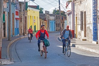 Cuban men riding on bicycles through colourful street in the old town centre of the city Camagueey on the island Cuba