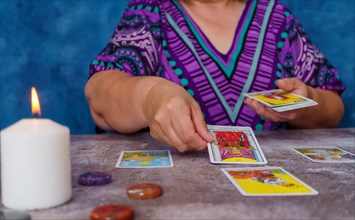 Unrecognizable woman casting tarot cards on the table candles and chakra stones