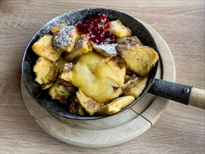 Cast iron frying pan with handle with classic dish from alpine cuisine Kaiserschmarrn sprinkled with icing sugar