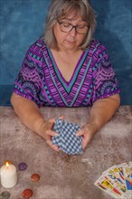 Woman shuffling tarot cards on a table with candles and chakra stones