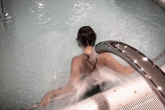 Woman Relaxing in a Hydro Massage Pool with Falling Water on Her Spine and Neck in Switzerland