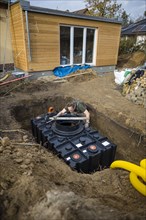 A man installs a water cistern in the garden next to his house to be able to water his garden with rainwater. Berlin