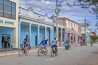 Cubans riding bicycles through street with colourful buildings in the city Ciego de Avila on the island Cuba
