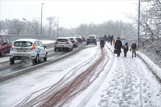 Cars and children walking to school over slippery pavement on bridge covered in sleet during unexpected late snow shower in March 2023