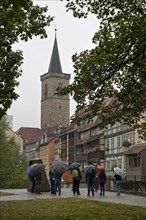 Group of people in the rain in front of half-timbered houses of the Kraemerbruecke and the Aegidienkirche
