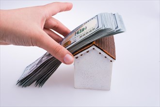 Hand holding American dollar banknotes on the roof of a model house on white background