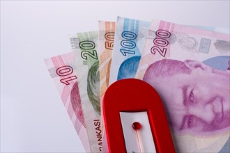 Turkish Lira banknotes by the side of a red color temperature on white background