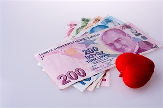 Turkish Lira banknotes by the side of a red color heart shaped object on white background