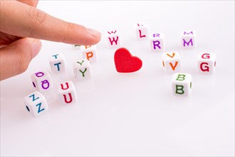 Hand pointing at Heart between Letter cubes on a white background