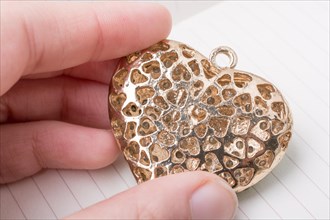 Heart shaped gold color metal object in hand