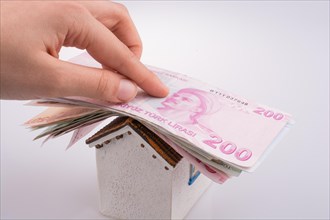 Hand holding Turkish Lira banknotes on the roof of a model house on white background
