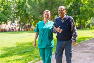 An elderly man with the nurse on a walk through the garden of a nursing home