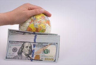 Human hand holding a model globe by the side of aAmerican dollar banknotes on white background