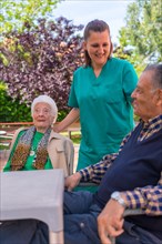 Two elderly people with the nurse in the garden of a nursing home or retirement home