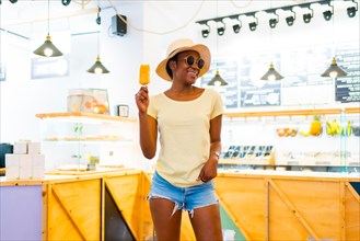 African black ethnicity woman eating a mango ice cream in a shop