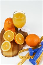 Natural orange juice with measuring tape and dumbbells on a wooden board and white background. concept fitnes weight loss