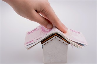 Hand holding Turkish Lira banknotes on the roof of a model house on white background