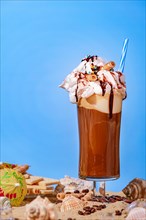 Iced coffee with whipped cream and chocolate sauce on sand