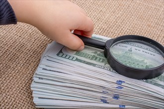 Toddler holding a magnifying glass over the banknote bundle of US dollar