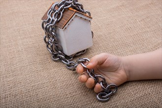 Little hand holding a chain around a model house on a brown background