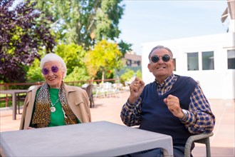 Two seniors dancing in the garden of a nursing home or retirement home at a summer party wearing sunglasses