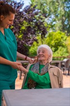An older or mature woman with the nurse in the garden of a nursing home in a moment of love and affection
