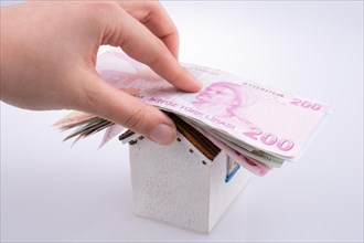 Hand holding Turkish Lira banknotes on the roof of a model house on white background