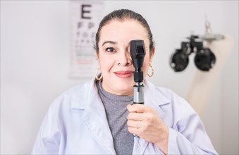 Portrait of female optometrist with ophthalmoscope in the laboratory. Smiling oculist holding an ophthalmoscope in the laboratory