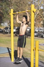 Young man doing pull ups on a crossbar at a park