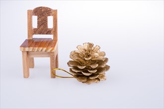 Pine cone bye the side of a model chair on a white background