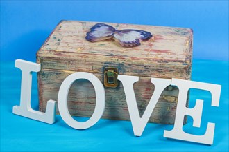 Word love written in white wooden letters on an antique wooden chest with a butterfly on top and a blue background