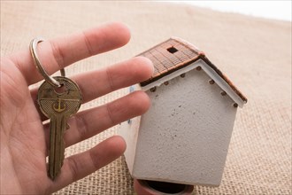 Hand holding a retro key by a model house on a brown color background