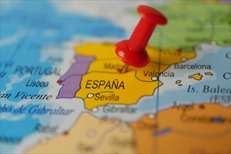 Spain marked with a red thumbtack on a map with an out-of-focus background