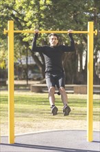 Young man doing pull ups on a crossbar at a park