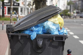Filled rubbish container with open flap standing by the road