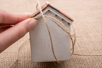 Hand holding a thread around a model house on a brown background