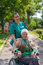 An elderly woman with the nurse on a walk in the garden of a nursing home in a wheelchair