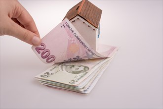 Hand holding Turkish Lira banknotes by the side of a model house on white background