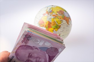 Turkish Lira banknotes by the side of a model globe on white background