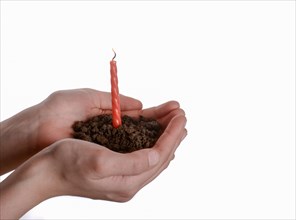 Cake candle in handful soil in hand on an isolated background