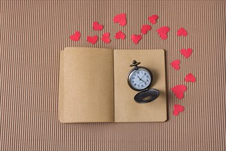 Retro Pocket watch on notebook with red paper hearts around