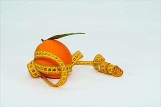Fresh orange with leaves surrounded by a tape measure isolated on white background and copy space