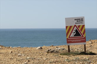 Warning sign of rockfall and falling rocks on a cliff on the rocky coast at Ponta da Sagres