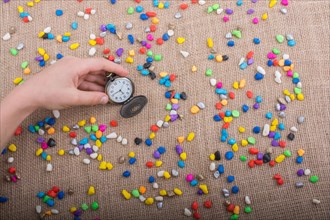 Pocket watch amid colorful pebbles on canvas background