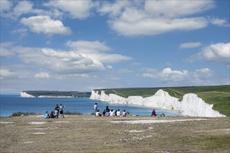 Tourists on the edge of the cliff looking towards The Seven Sisters chalk cliffs