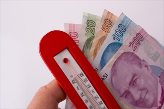 Turkish Lira banknotes by the side of a red color temperature on white background