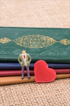 Man figurine beside a heart standing on little books