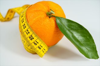 Fresh orange with leaves surrounded by a tape measure isolated on white background and copy space