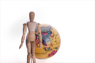 Wooden man standing in front of a globe on a white background