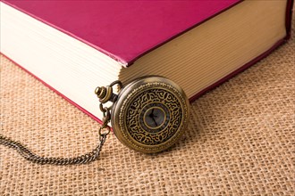 Retro style pocket watch beside a book on a canvas